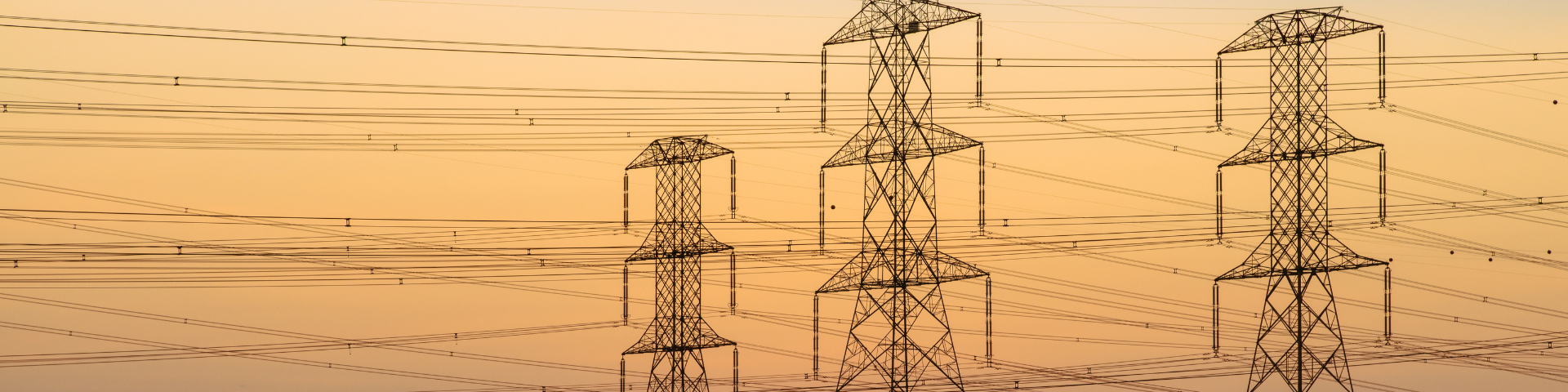 Transmission lines silhouetted by an orange sunset