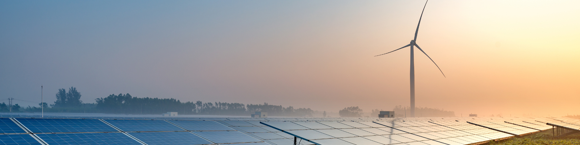 Rows of solar panels in the foreground and a wind turbine in the background at sunrise.