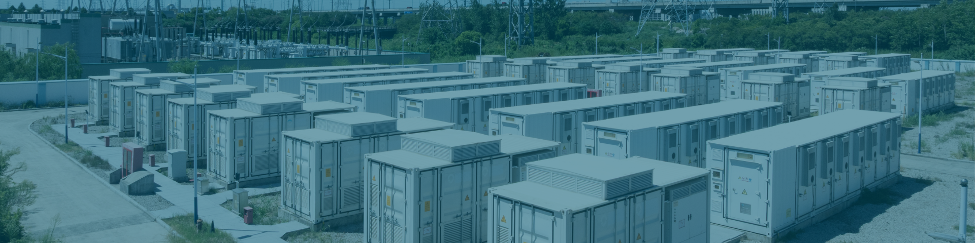 Aerial view of a large battery energy storage facility with rows of white and gray container-like buildings and utility structures